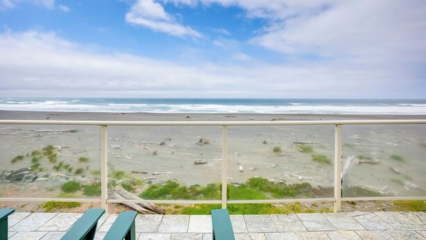 A beach view from a balcony with a railing, featuring a sandy beach with sparse vegetation and the ocean in the background. - Gold Beach Retreat: Private Hot Tub + Ocean Views! (Gold Beach)