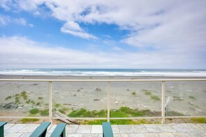 A beach view from a balcony with a railing, featuring a sandy beach with sparse vegetation and the ocean in the background. - Gold Beach Retreat: Private Hot Tub + Ocean Views! (Gold Beach)