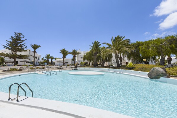 A swimming pool with a circular center, surrounded by palm trees and white buildings.