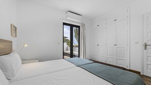A bedroom with a bed, a bedside table, a lamp, a wardrobe, and a sliding glass door leading to a balcony.
