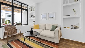 A modern living room with a sofa, a coffee table, a striped rug, and a window with a view of buildings outside.