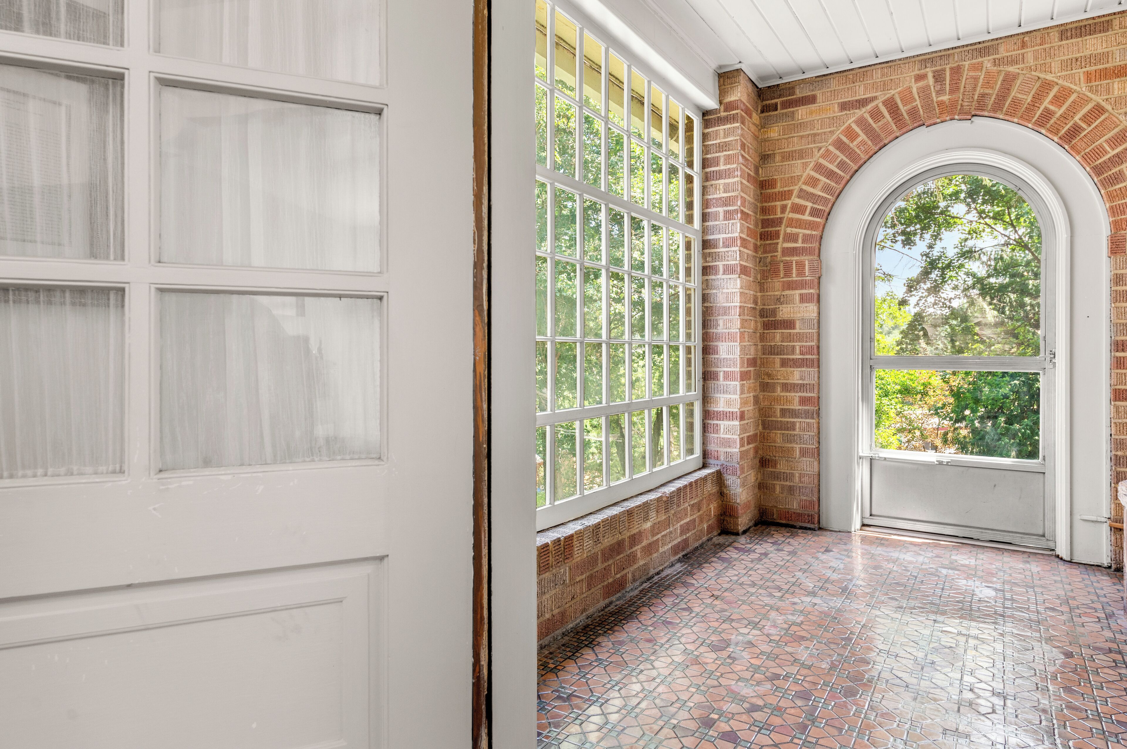 A room with a tiled floor, a white door, and a large window with a view of trees.