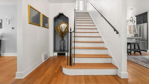 Una escalera de madera con barandilla negra que lleva a una plataforma con un jarrón y cuadros enmarcados.