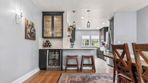 Una cocina moderna con armarios oscuros, un refrigerador de acero inoxidable y una mesa de comedor de madera con taburetes.