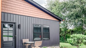A modern building with a dark exterior, a front door, and a small patio area with two chairs and a table.