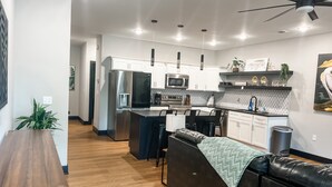 A modern kitchen with stainless steel appliances, a central island, and a seating area with a black leather couch.