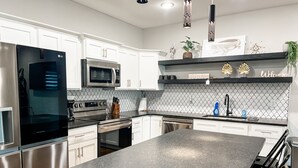 A modern kitchen with stainless steel appliances, white cabinetry, and a black granite countertop.