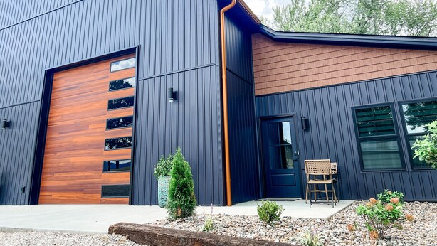 A modern building with a large garage door, a small porch with a bench, and a garden area with plants and pebbles.