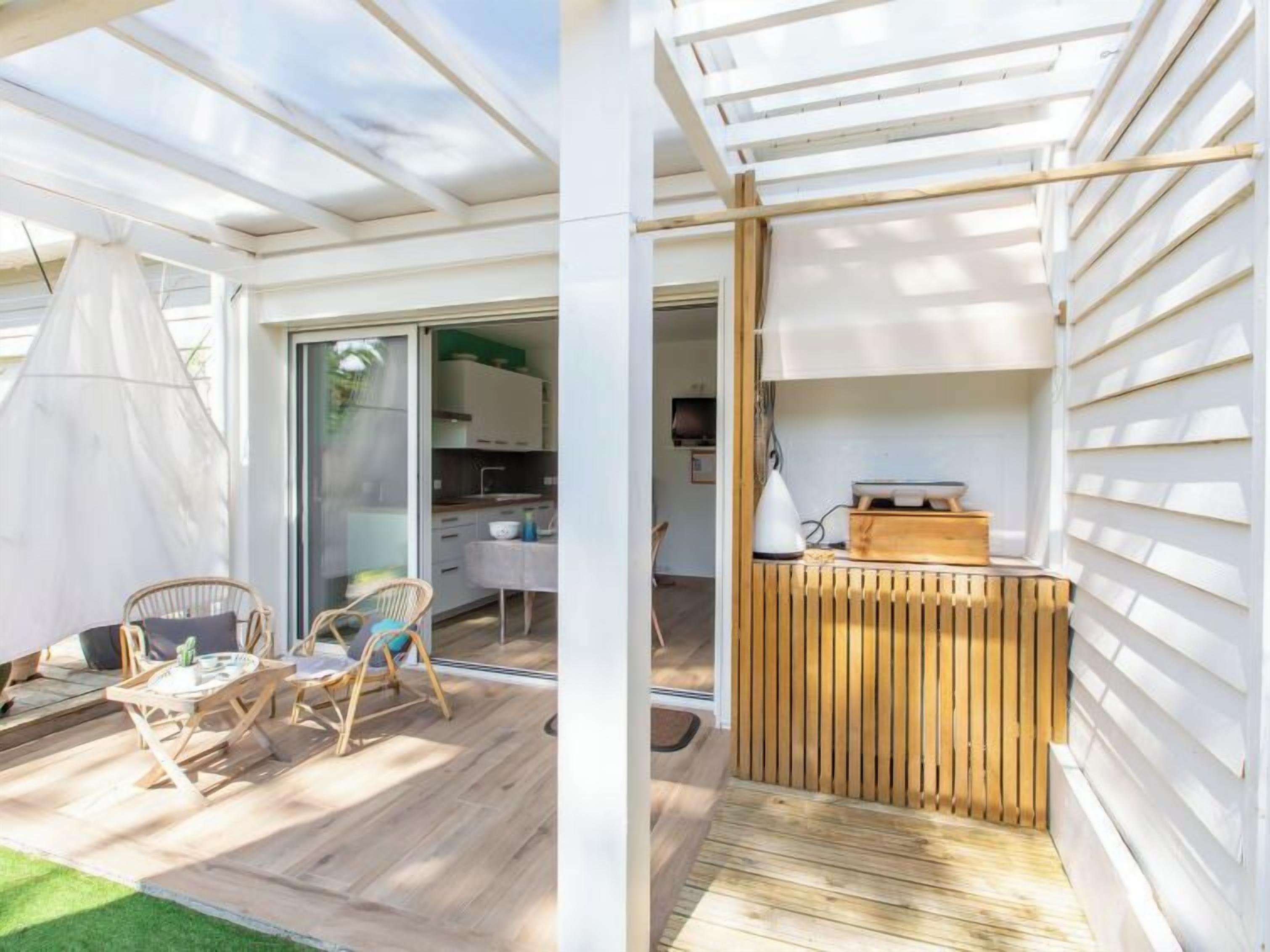 Un espacio habitable moderno y de concepto abierto, con piso de madera, un comedor con sillas de mimbre, una zona de cocina y un gran ventanal corredero que da a un patio.