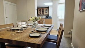 A dining table set with plates, glasses, and cutlery, with a vase of flowers in the center. - Bay Tree Cottage (Keswick)