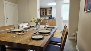 A dining table set with plates, glasses, and cutlery, with a vase of flowers in the center. - Bay Tree Cottage (Keswick)