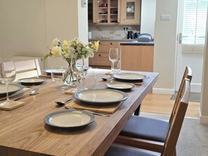 A dining table set with plates, glasses, and cutlery, with a vase of flowers in the center. - Bay Tree Cottage (Keswick)