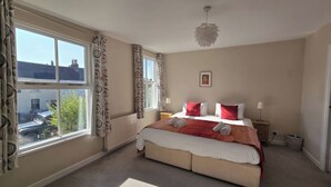 A bedroom with a large window, a bed with red and white bedding, a bedside table with a lamp, and a ceiling light fixture. - Bay Tree Cottage (Keswick)