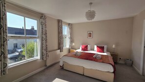 A bedroom with a large window, a bed with red and white bedding, a bedside table with a lamp, and a ceiling light fixture. - Bay Tree Cottage (Keswick)