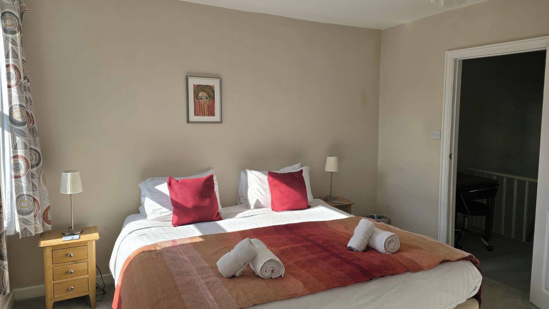 Ein Hotelzimmer mit einem Bett, zwei Nachttischen, einer Lampe, einem gerahmten Bild an der Wand und einer Tür, die auf einen Balkon führt.