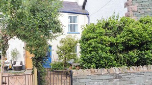 A residential property with a stone wall, a blue door, and a garden area. - Bay Tree Cottage (Keswick)
