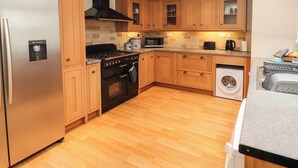 A modern kitchen with wooden cabinets, a stainless steel refrigerator, a stove, a microwave, and a washing machine. - Bay Tree Cottage (Keswick)