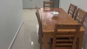 Een eethoek met een houten tafel en stoelen, een keuken op de achtergrond en een klok aan de muur.