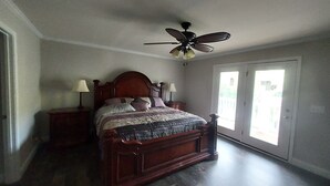 Een slaapkamer met een houten bed, twee nachtkastjes met lampen, een plafondventilator en een schuifdeur van glas naar een balkon.