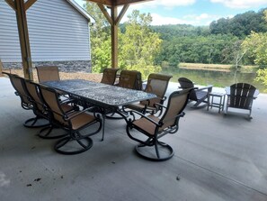 Eine Terrasse im Freien mit Tisch und Stühlen, ein überdachter Sitzbereich und Blick auf See und Wald.