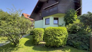 Ein zweistöckiges Haus mit Balkon, umgeben von gepflegter Bepflanzung und blauem Himmel.