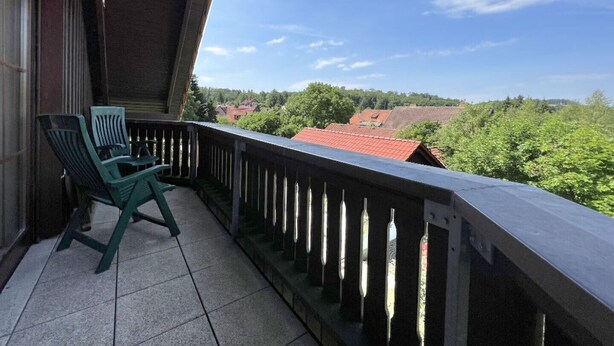 Ein Balkon mit Blick auf ein Dorf, ein Stuhl und ein Fliesenboden.