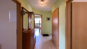 Ein Flur mit einer Holztür rechts, einem Holzschrank links und einer Leuchte an der Decke.