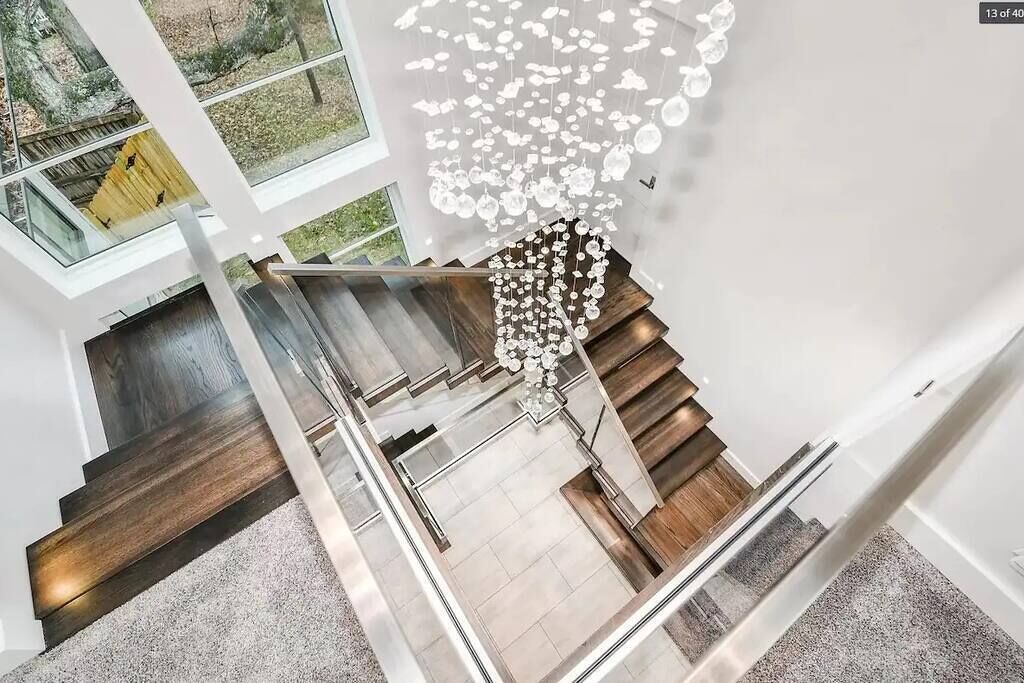 A modern interior with a staircase, glass railings, and a decorative hanging light fixture.