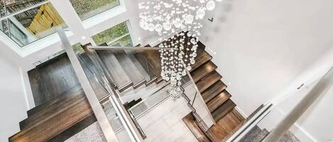 A modern interior with a staircase, glass railings, and a decorative hanging light fixture.