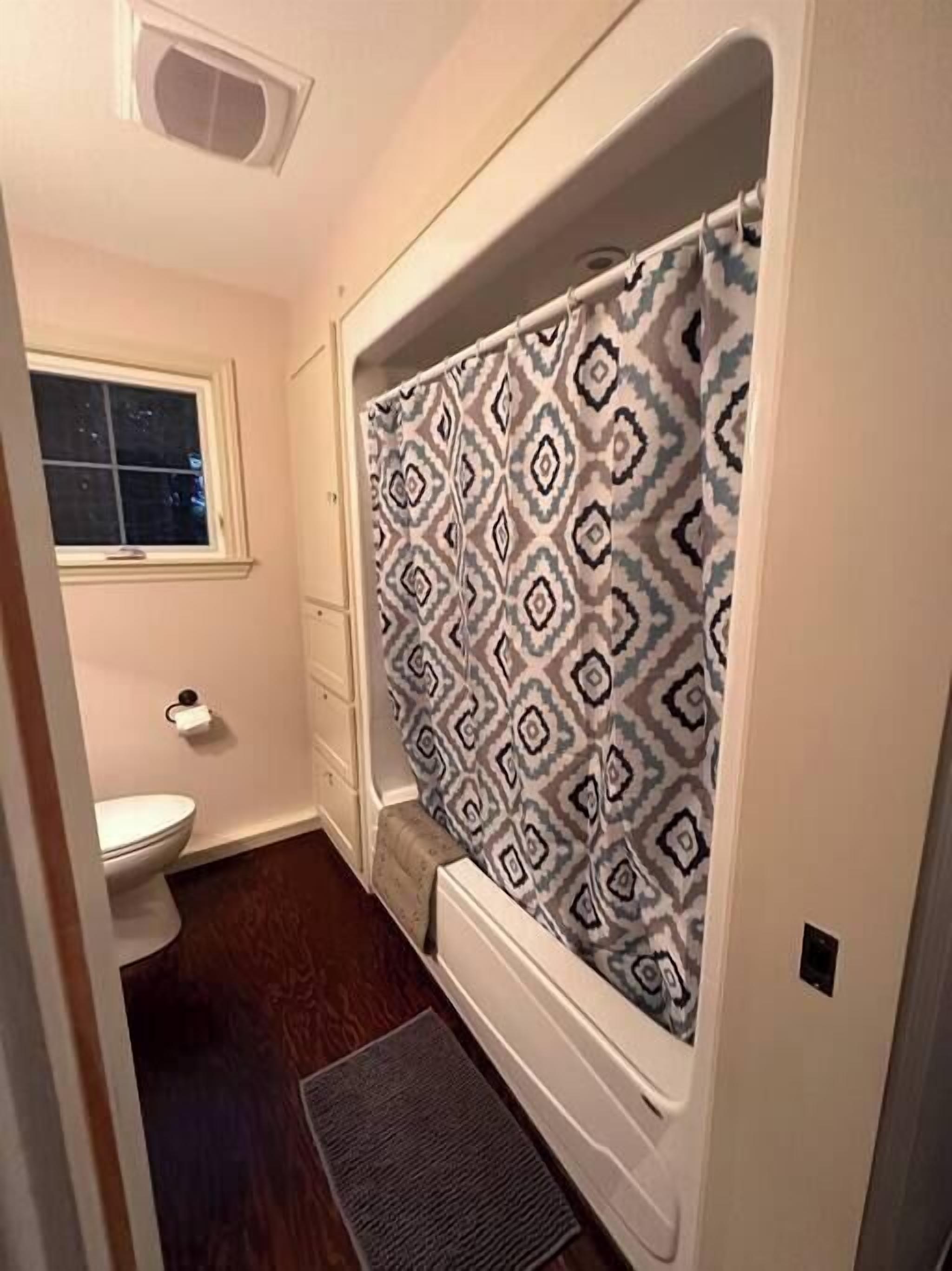 A small bathroom with a toilet, a shower with patterned curtain, and a window.