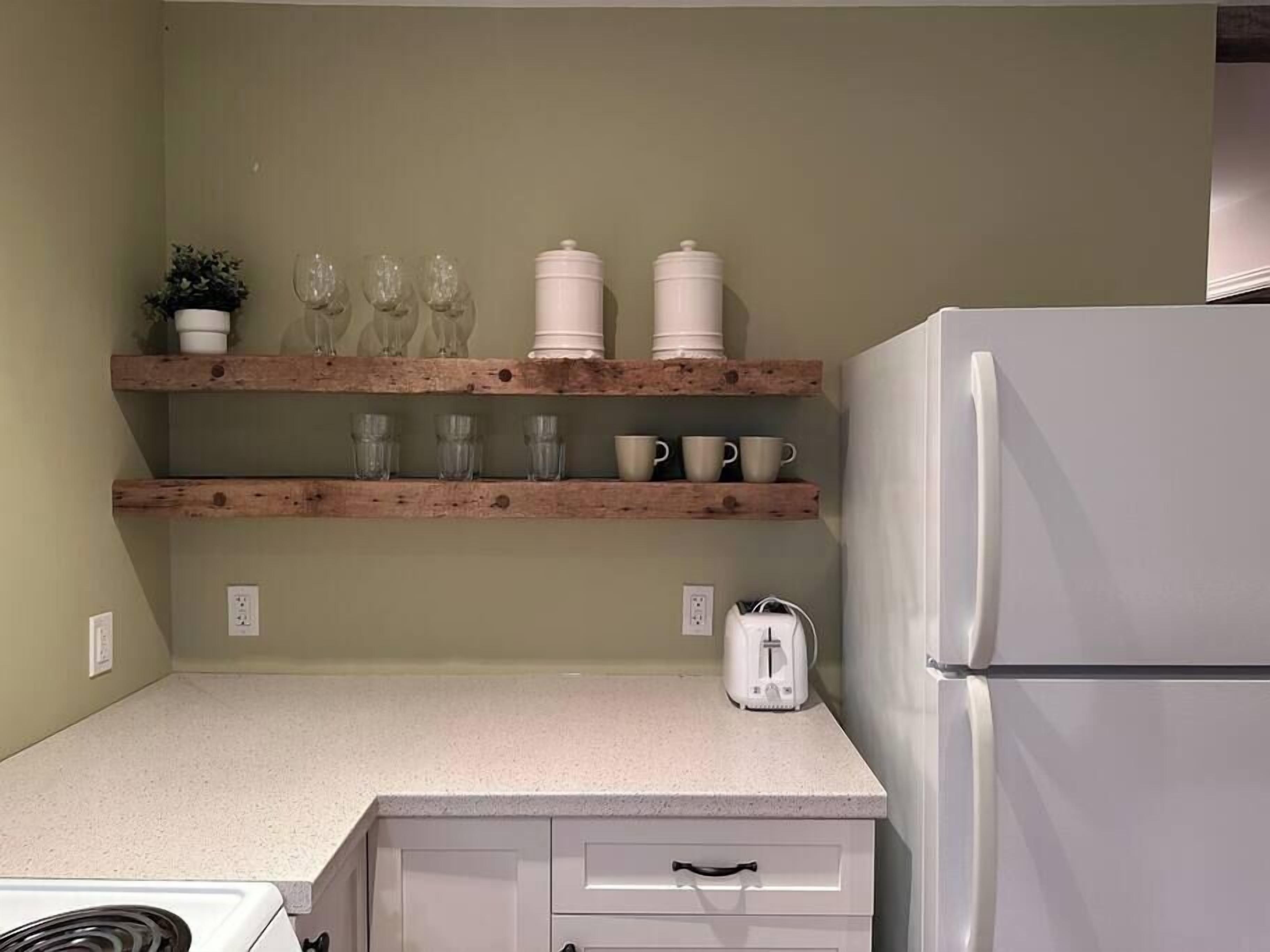 A kitchen with wooden shelves holding glassware, cups, and a toaster.