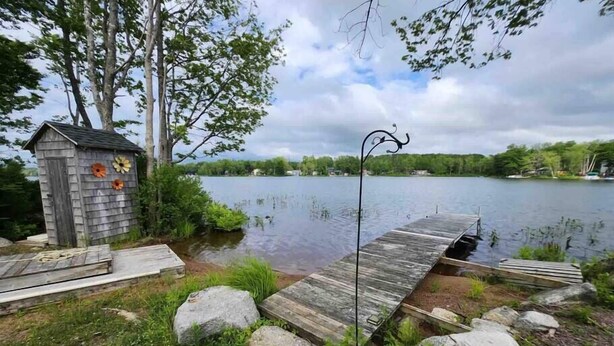 Une jetée en bois s’étendant sur un lac paisible, entourée de rochers et de verdure.
