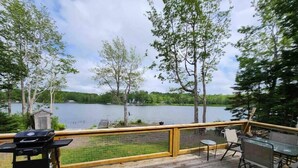 Une terrasse en bois avec un barbecue, des chaises et une table, le tout donnant sur un lac.