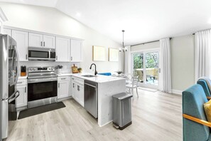 A modern kitchen with stainless steel appliances, a central island, and a dining area with a view of the outdoors. - Waterfront Home w/Private Hot Tub · Game Room · Fire Pit · Kayaks (Montross)