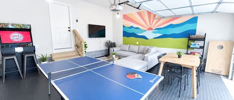 A ping pong table in a room with a sofa, a TV, and a colorful mural on the wall.