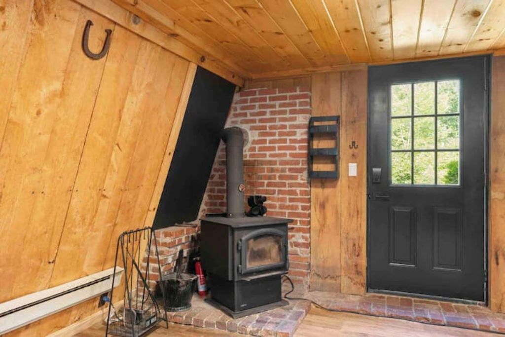 Un interior de madera con una puerta negra, una chimenea de ladrillo y un perchero metálico.
