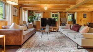 A cozy cabin-style room with two sofas, a television, and a large window. - A-Frame Hot tub Retreat - Firepit, Grill, EV & Dog Friendly, Close to N. Conway. (Fryeburg)