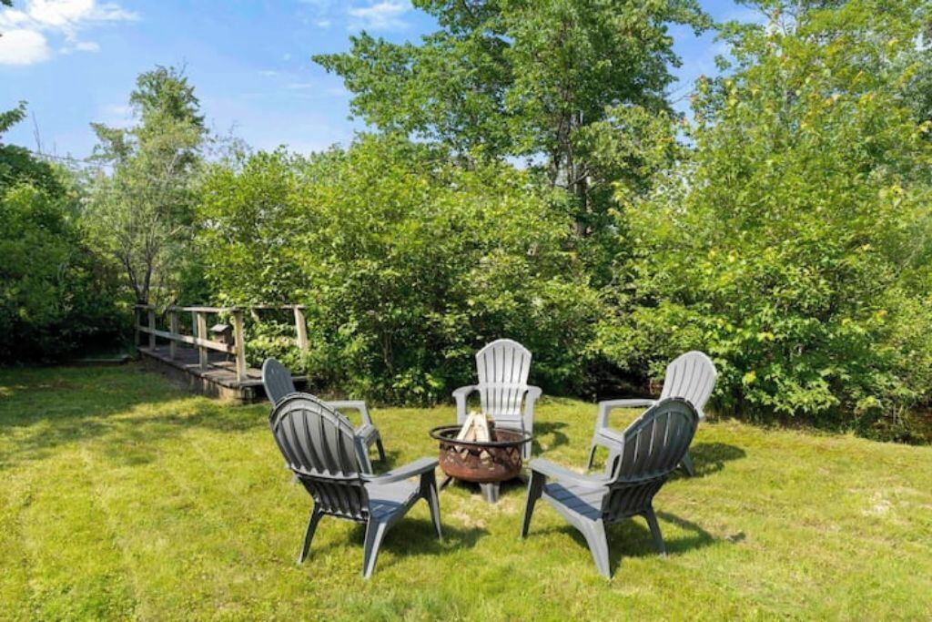 A backyard with a fire pit and Adirondack chairs.