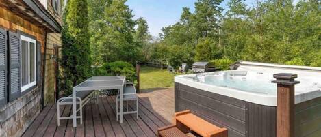A wooden deck with a hot tub, a table, and a bench.