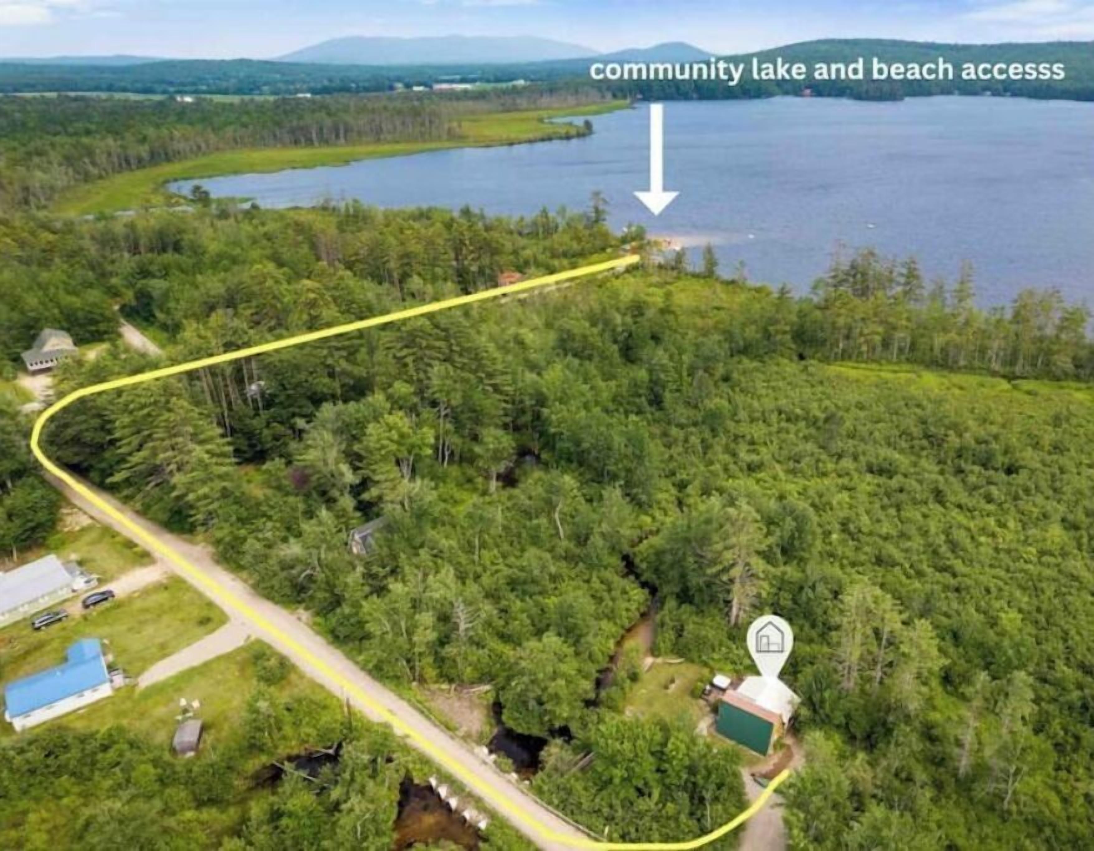 Vista aérea de um lago comunitário e acesso à praia, com um caminho amarelo sinuoso.