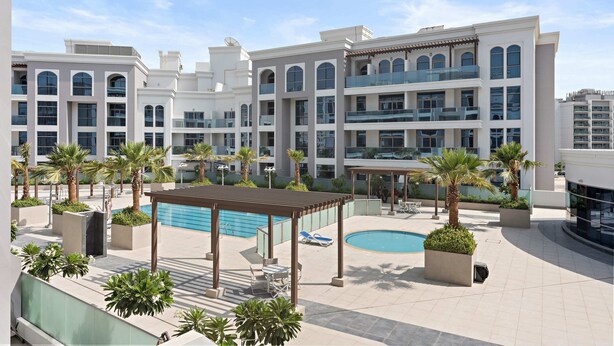 Un hotel moderno con piscina en la azotea, mobiliario exterior y palmeras.