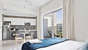 Una habitación de hotel moderna con una cama grande, un balcón con vistas, una kitchenette y un comedor.