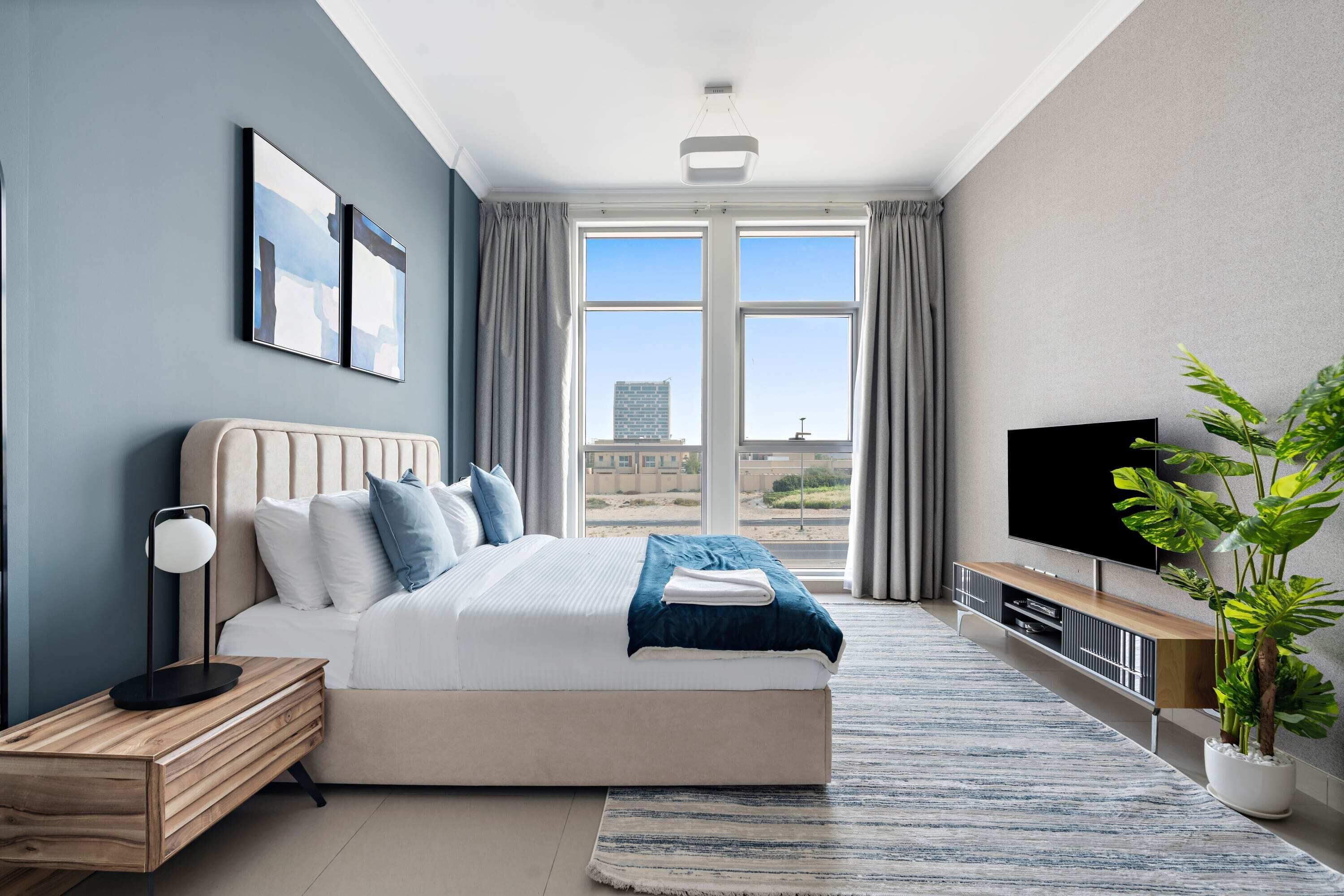 Ein modernes Schlafzimmer mit einem großen Bett, einem Fernseher, einer Pflanze und Blick auf die Stadt.