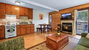 A modern kitchen with wooden cabinets, a stone backsplash, and a built-in oven. There is a dining area with a table and chairs, and a living room with a sofa and a fireplace. - Alpine Alcove Near Kings Beach - Private Sleeping Nook - Pet Friendly (Tahoe Vista)