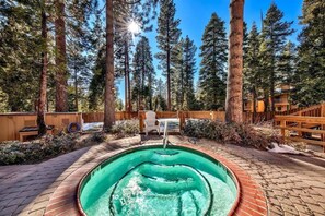 Un jacuzzi rodeado por una terraza de madera, con una valla de madera y altos árboles al fondo.