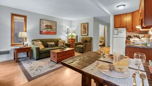 A living room with a green sofa, wooden coffee table, and a dining table set for a meal. - Alpine Alcove Near Kings Beach - Private Sleeping Nook - Pet Friendly (Tahoe Vista)