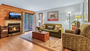 A living room with a fireplace, green sofa, and a television mounted on the wall. - Alpine Alcove Near Kings Beach - Private Sleeping Nook - Pet Friendly (Tahoe Vista)