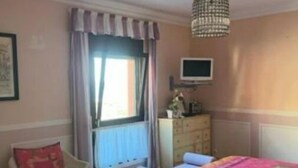 A bedroom with a bed, a chair, a dresser, a TV, and a window with curtains.