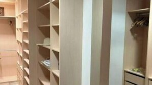 A walk-in closet with open shelving and drawers, light-colored walls, and a tiled floor.