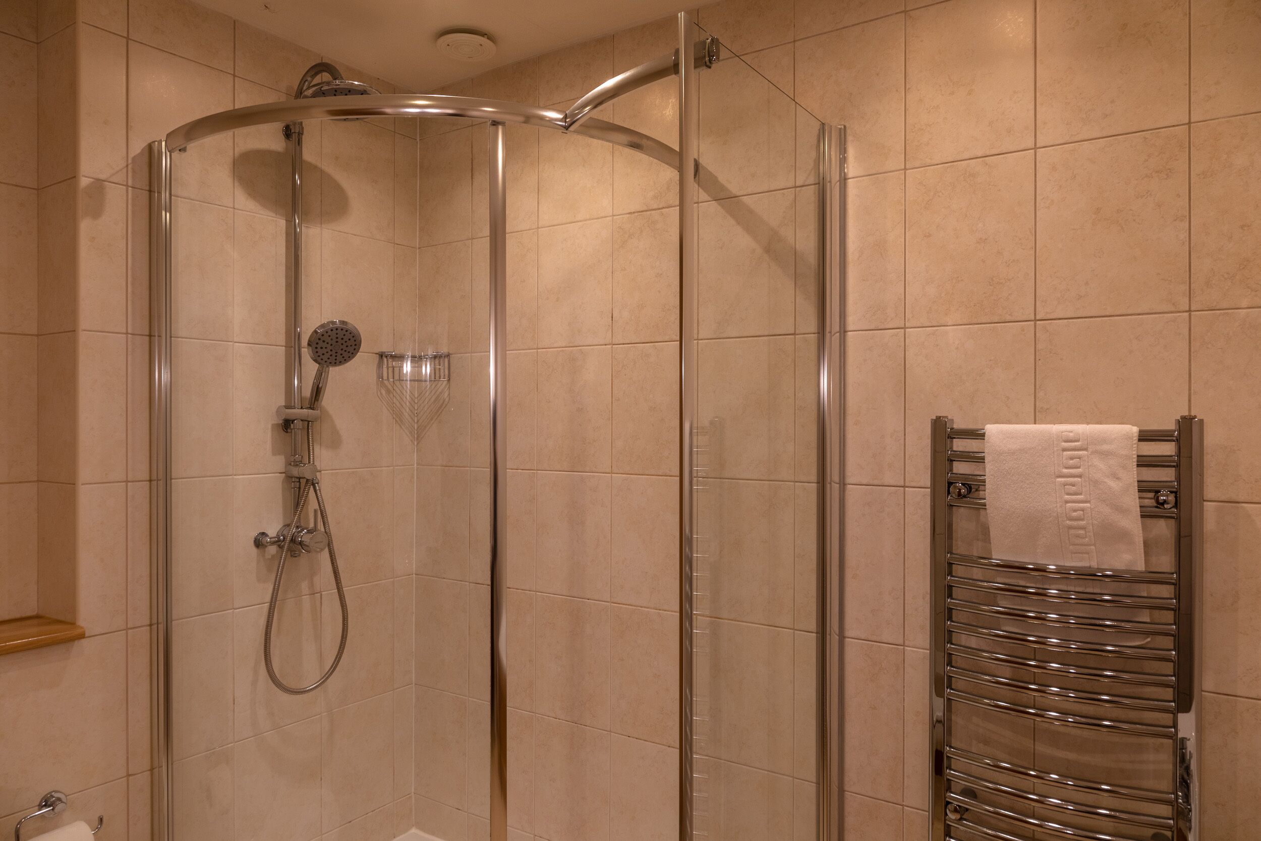 Eine begehbare Dusche mit Glaswänden, einer Handbrause und einem am Wand montierten Wasserhahn.
